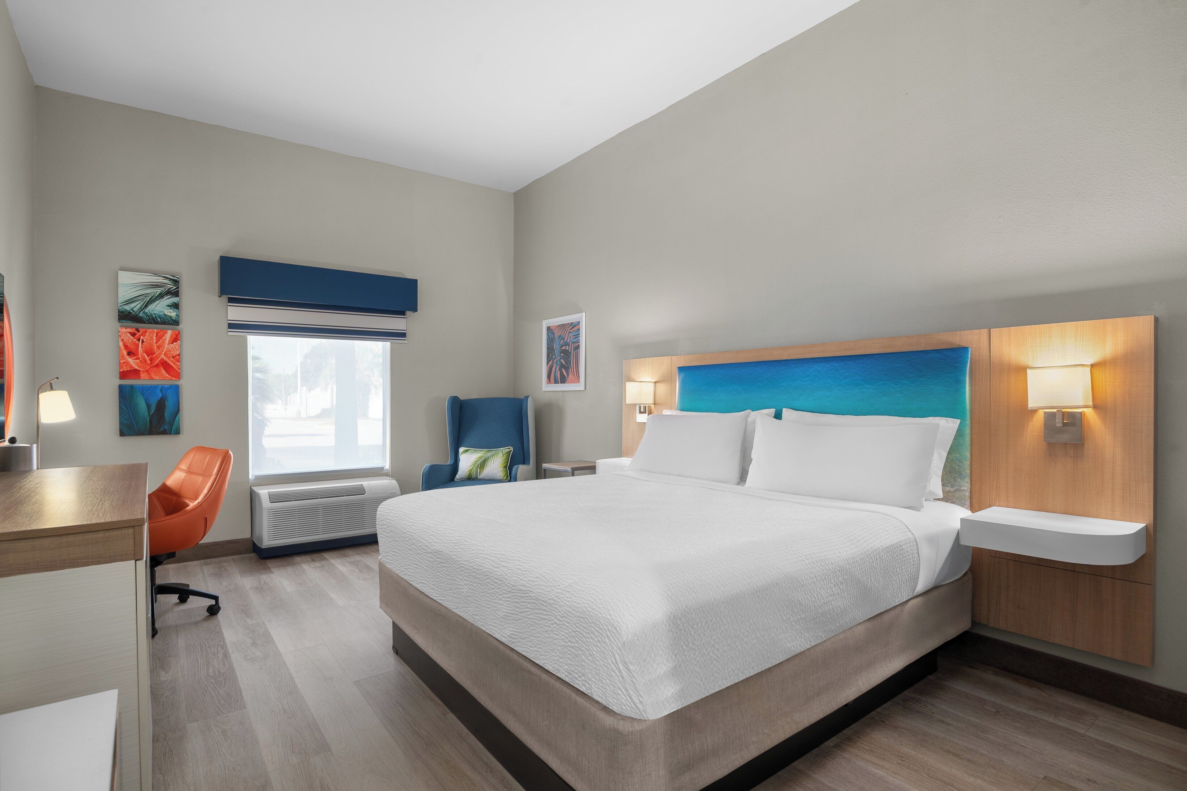 Una habitación de hotel moderna con una cama grande, un escritorio, una silla y una ventana con persianas.