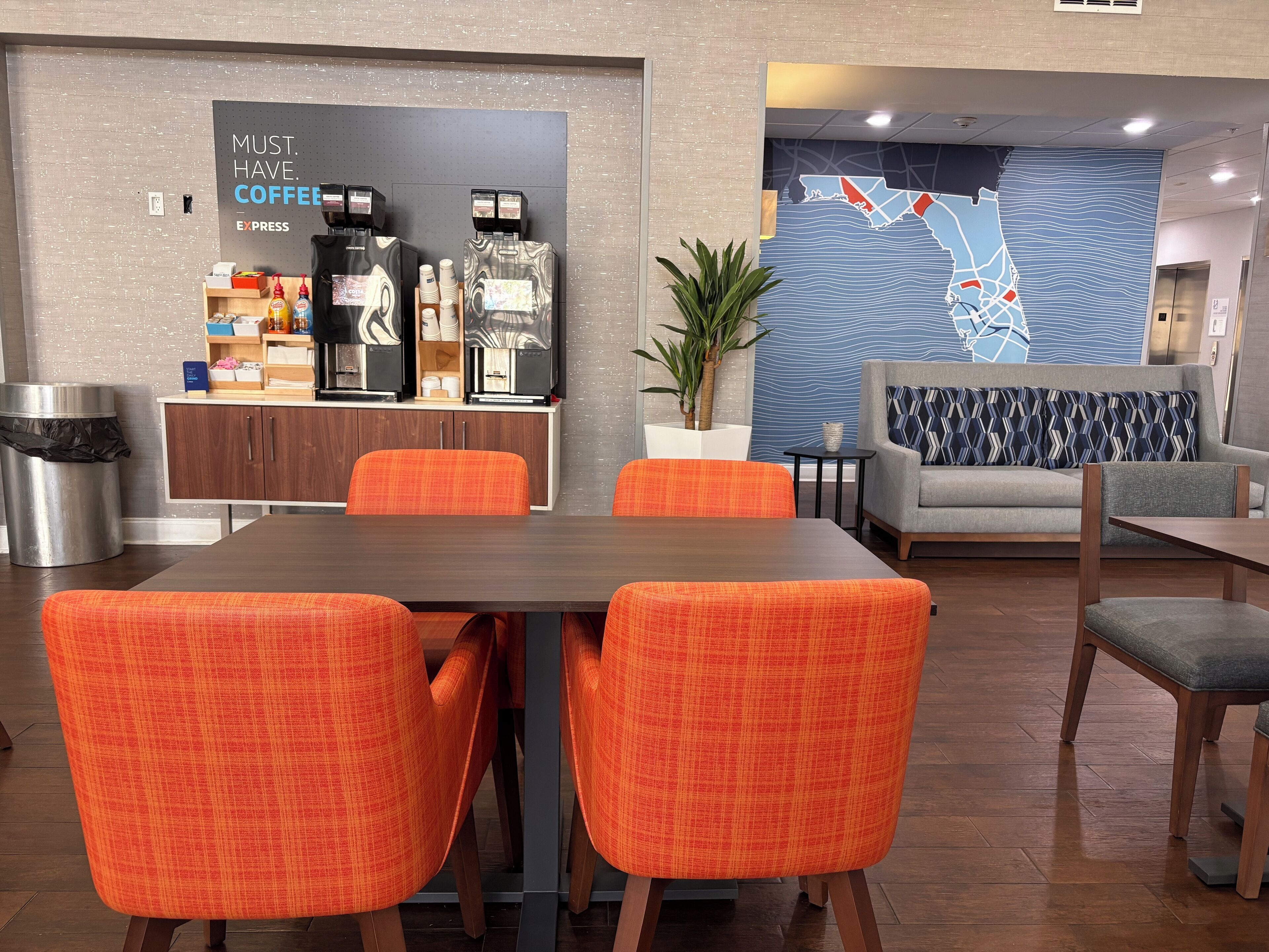 A modern hotel lobby with a coffee bar, seating area, and a map on the wall.