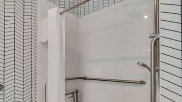 A shower area with white tiled walls, a metal grab bar, and a showerhead.