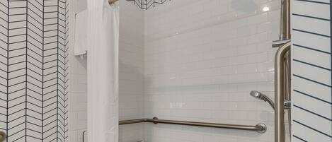 A shower area with white tiled walls, a metal grab bar, and a showerhead.