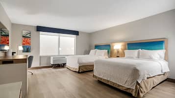 A hotel room with two beds, a desk, and a large window.