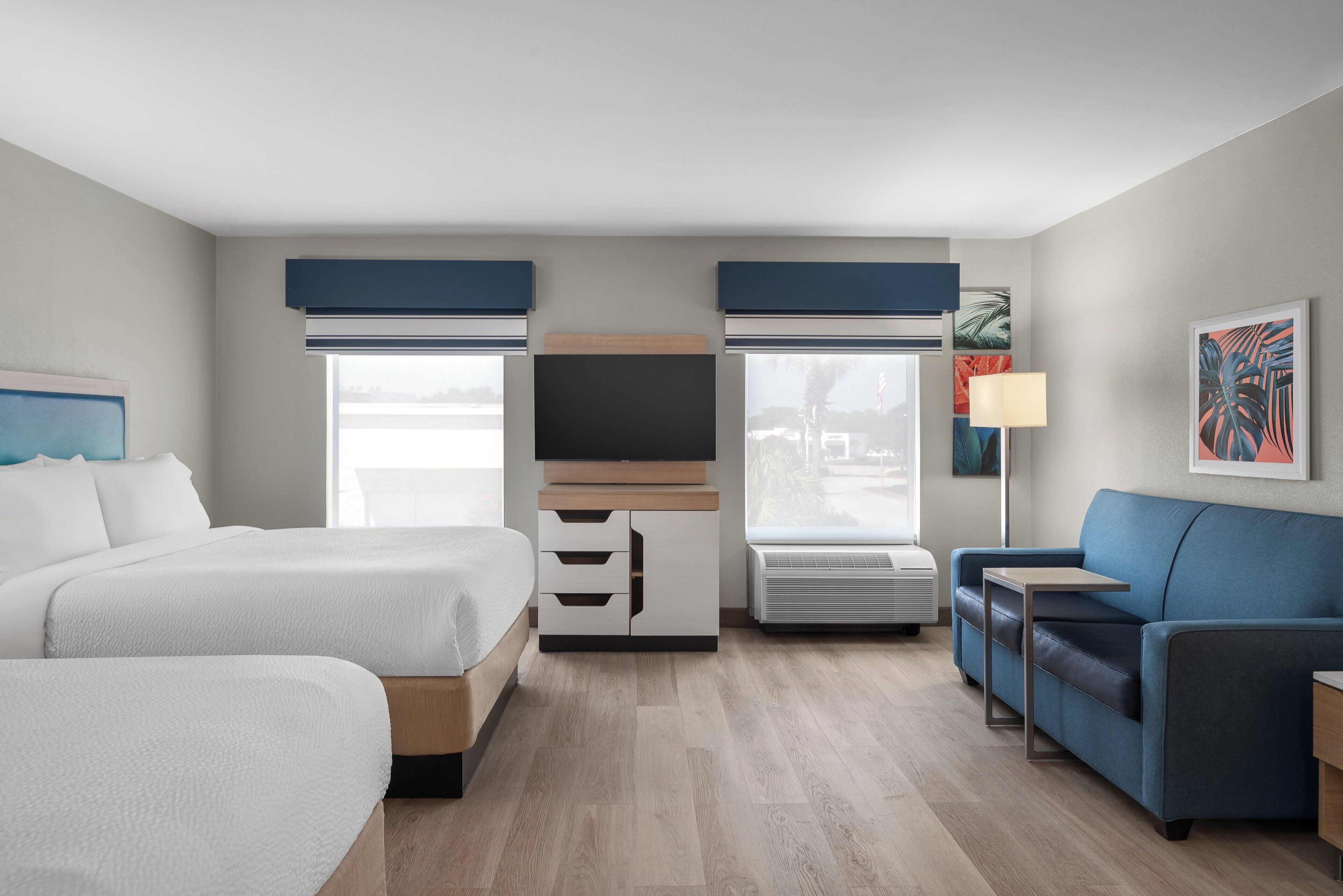 Une chambre d’hôtel avec deux lits, un canapé, une télévision et une fenêtre avec des stores.