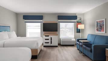 Une chambre d’hôtel avec deux lits, un canapé, une télévision et une fenêtre avec des stores.
