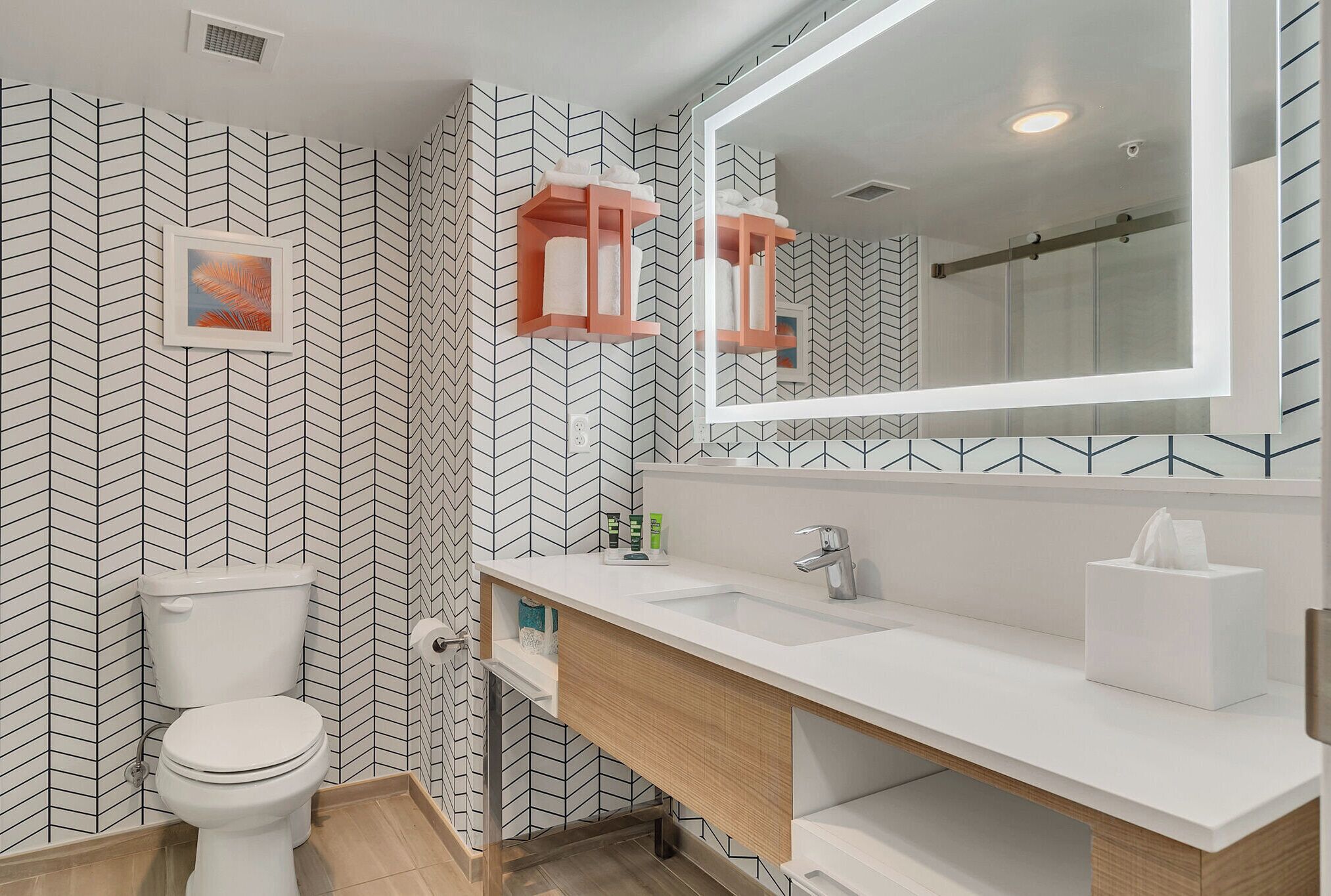Une salle de bain moderne avec un mur orné d’un motif en chevrons noir et blanc, un meuble-lavabo en bois, un grand miroir et des toilettes.
