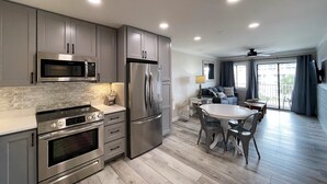 A modern kitchen with stainless steel appliances, a dining area with a table and chairs, and a balcony with a view.