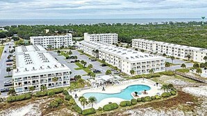 A resort with multiple white buildings, a central swimming pool, and a beach area.