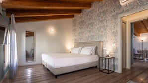 A bedroom with a large bed, wooden flooring, a patterned wall, and a small bedside table with a lamp. - Palazzina Riello (Venice)