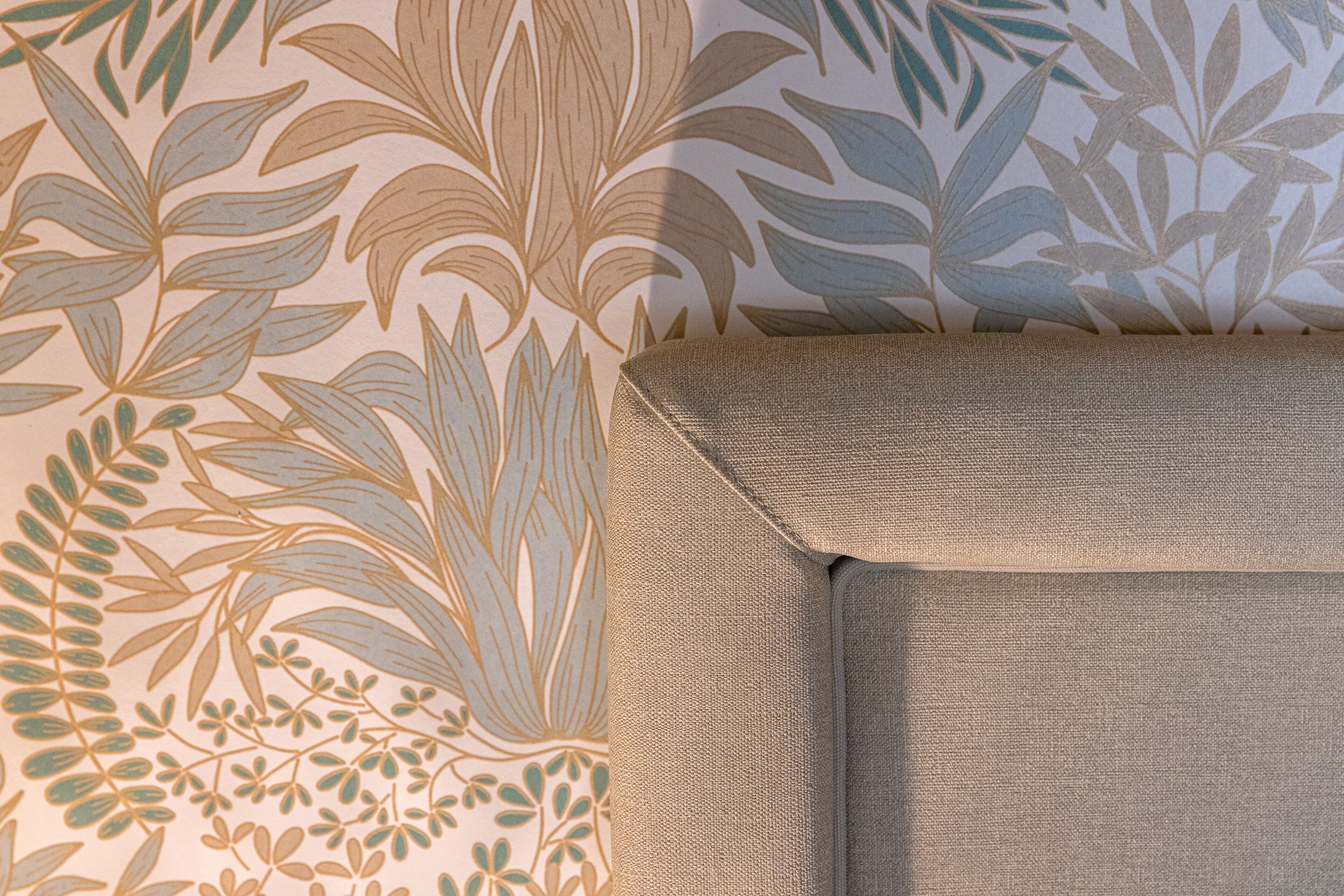 A wall with a floral pattern and a section of a beige sofa.