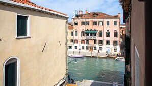 A narrow canal with boats, buildings with balconies, and a wooden bench. - Palazzina Riello (Venice)