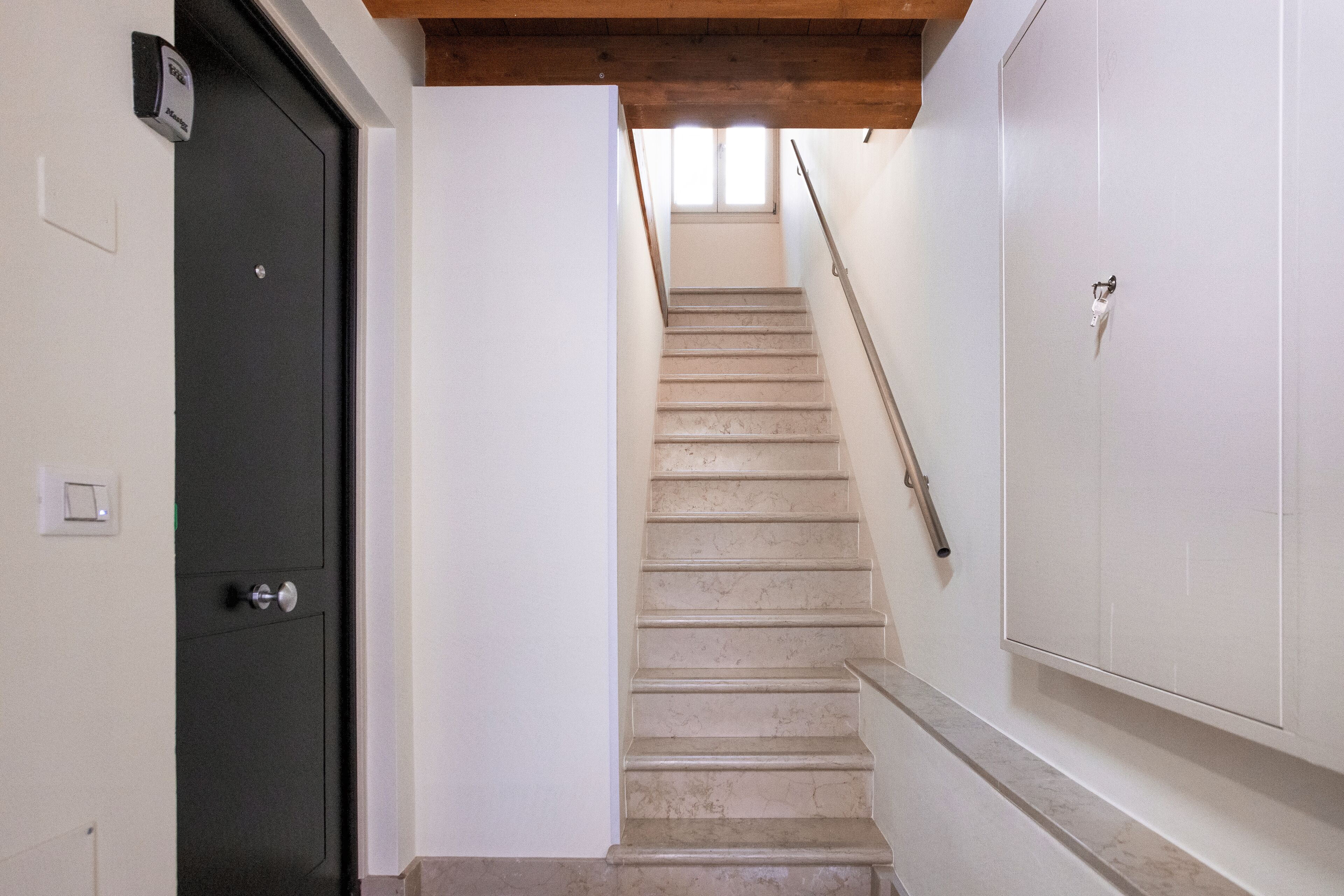 A staircase with a handrail, a door on the left, and a wall with a light switch.