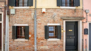 A brick building with two windows, a door, and a small balcony. - Palazzina Riello (Venice)