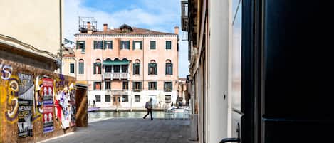 A narrow street with a canal, buildings with balconies, and a person walking.