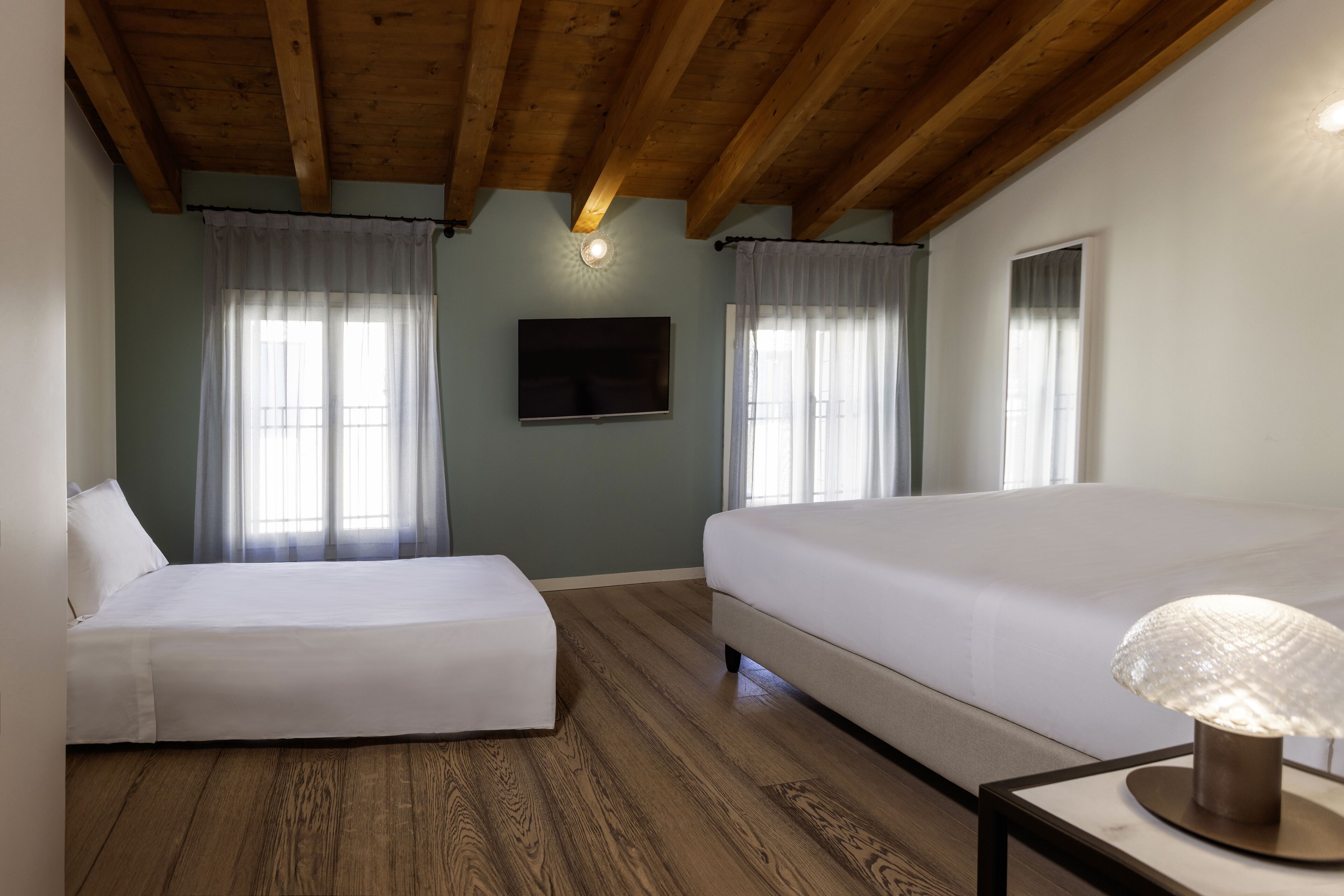Ein Schlafzimmer mit zwei Betten, Holzboden, Deckenventilator und einem angebrachten Fernseher.