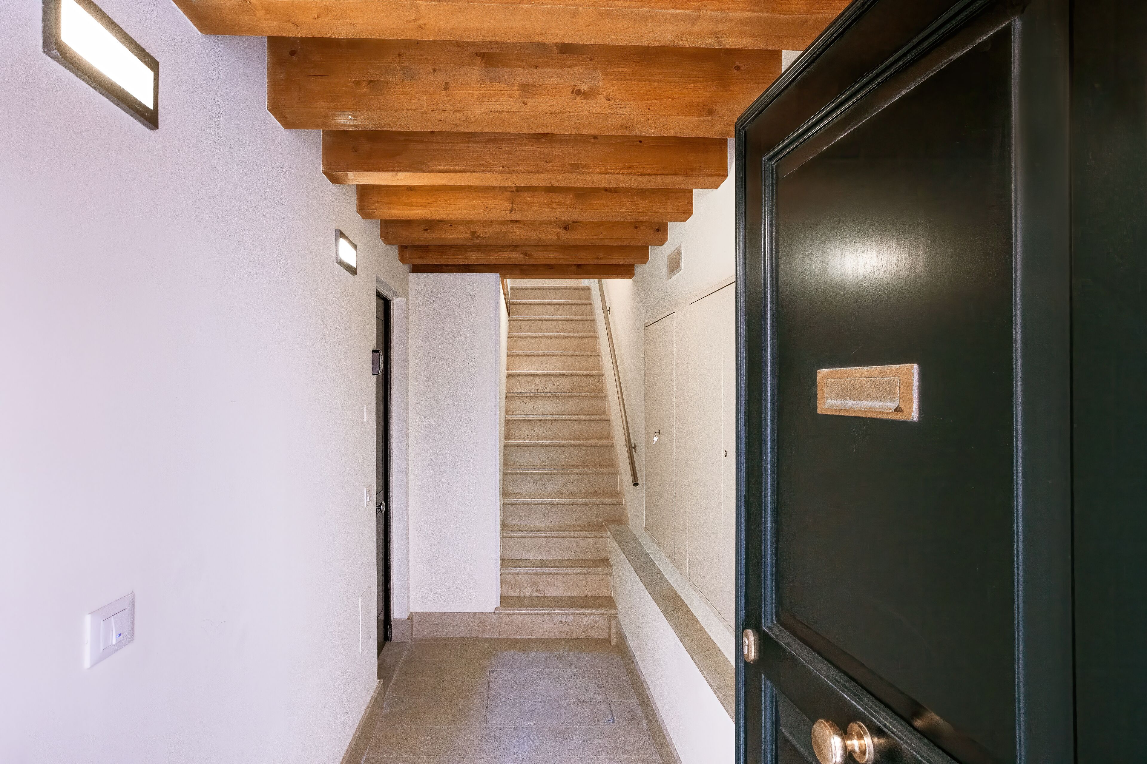 A hallway with a wooden ceiling, a dark door with a nameplate, and a staircase in the background.