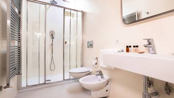 Un baño moderno con ducha de vidrio, lavamanos blanco y bidé.