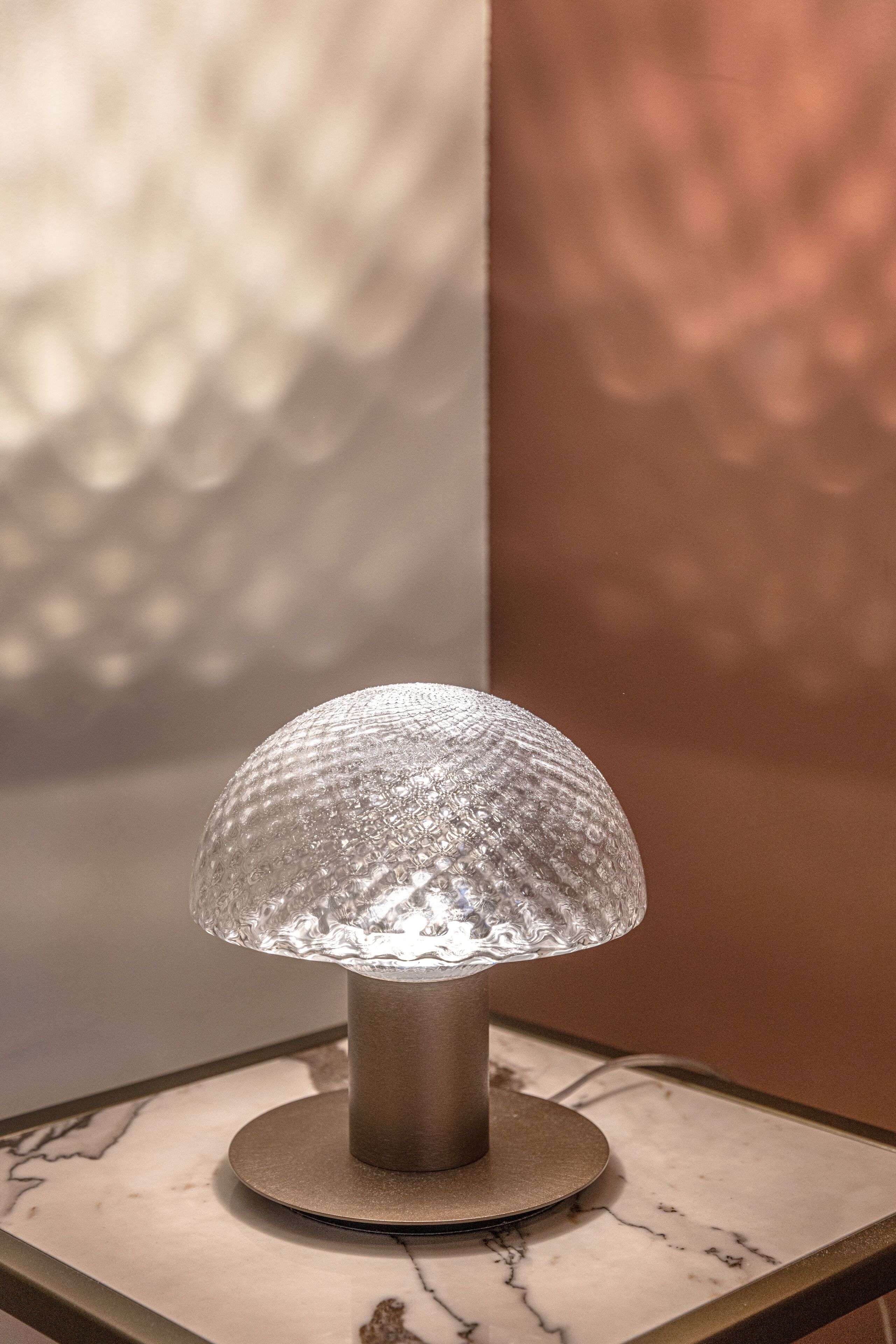 A table lamp with a textured glass shade on a marble table.