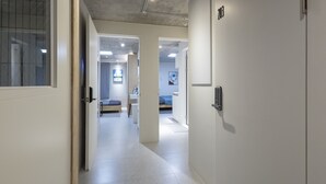 Un pasillo que conduce a un dormitorio con una cama, una mesita de noche y un televisor montado en la pared.