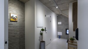 Un pasillo moderno con pared de hormigón, una planta en maceta, una puerta y un ventanal pequeño.