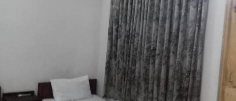 A bedroom with two single beds, a wooden headboard, a nightstand, a wall-mounted air conditioner, and a window with grey curtains.