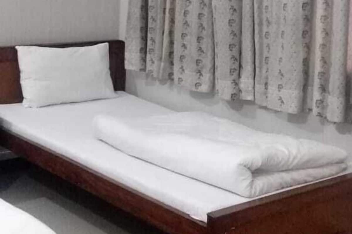 Una cama individual con estructura de madera, ropa de cama blanca y cortina gris con estampado.