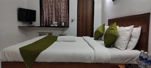 A hotel room with a bed, pillows, a television, a window with curtains, and a bedside table with a bottle. - Calangute Villae By Urban Getaway (Calangute)