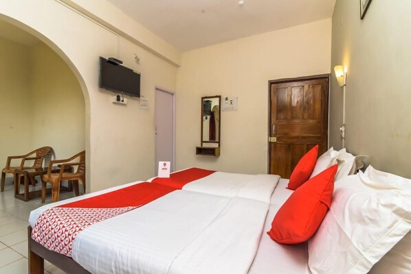 A hotel room with a bed, a television mounted on the wall, a wooden door, and a small seating area with chairs. - Calangute Villae By Urban Getaway (Calangute)