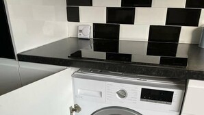 Eine kompakte, weiße Waschmaschine mit Frontlader in einer modernen Küche mit schwarz-weißen Fliesen und einer schwarzen Arbeitsplatte.