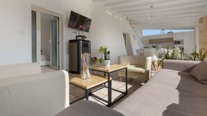 A modern living room with a sofa, a coffee table, and a TV mounted on the wall. There is a kitchen area visible through an open door. - 3191 Villa Sergi by Perle di Puglia (Gagliano del Capo)