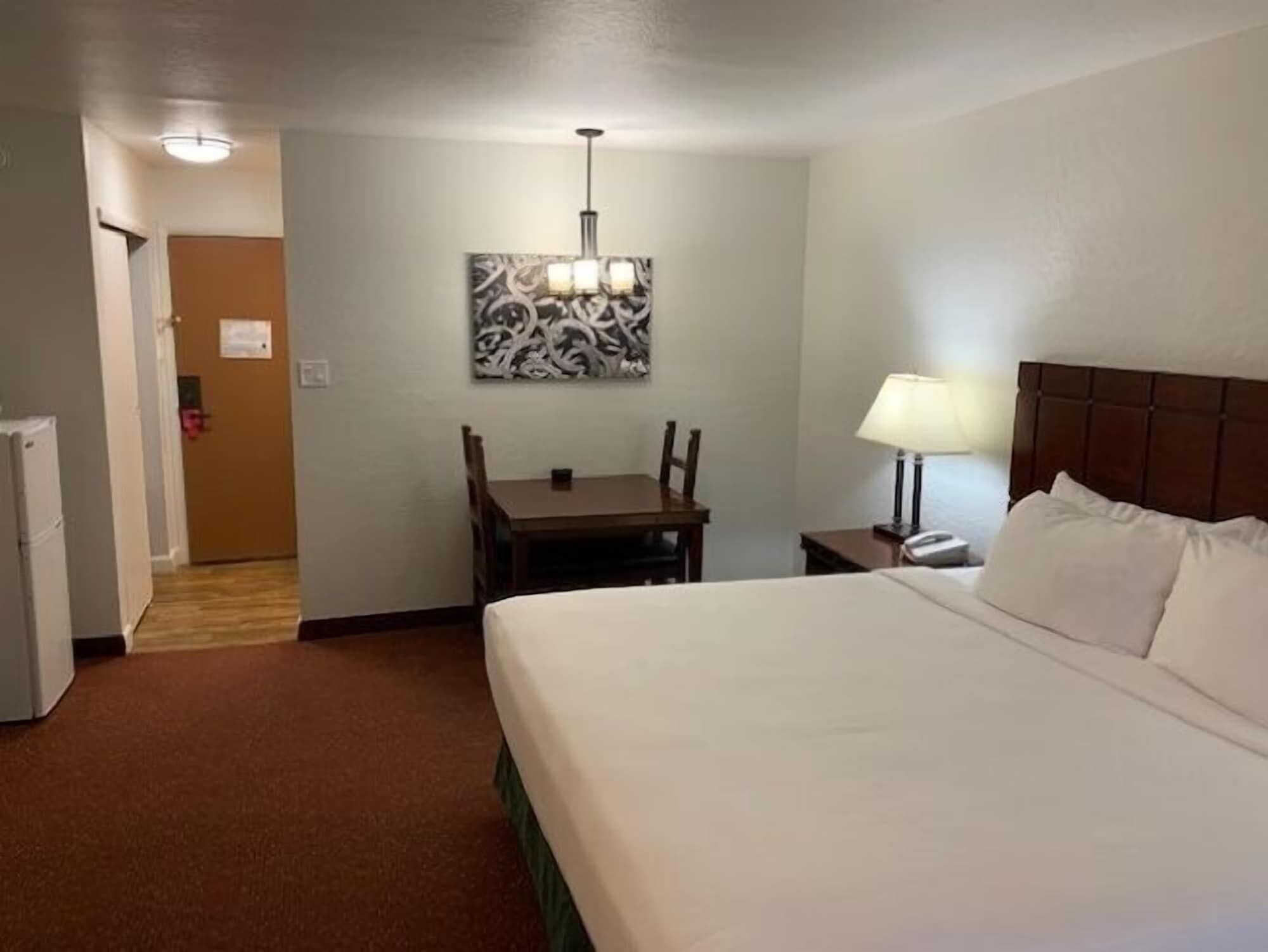 Une chambre d’hôtel avec un lit, un bureau, une chaise, une lampe et un tableau au mur.