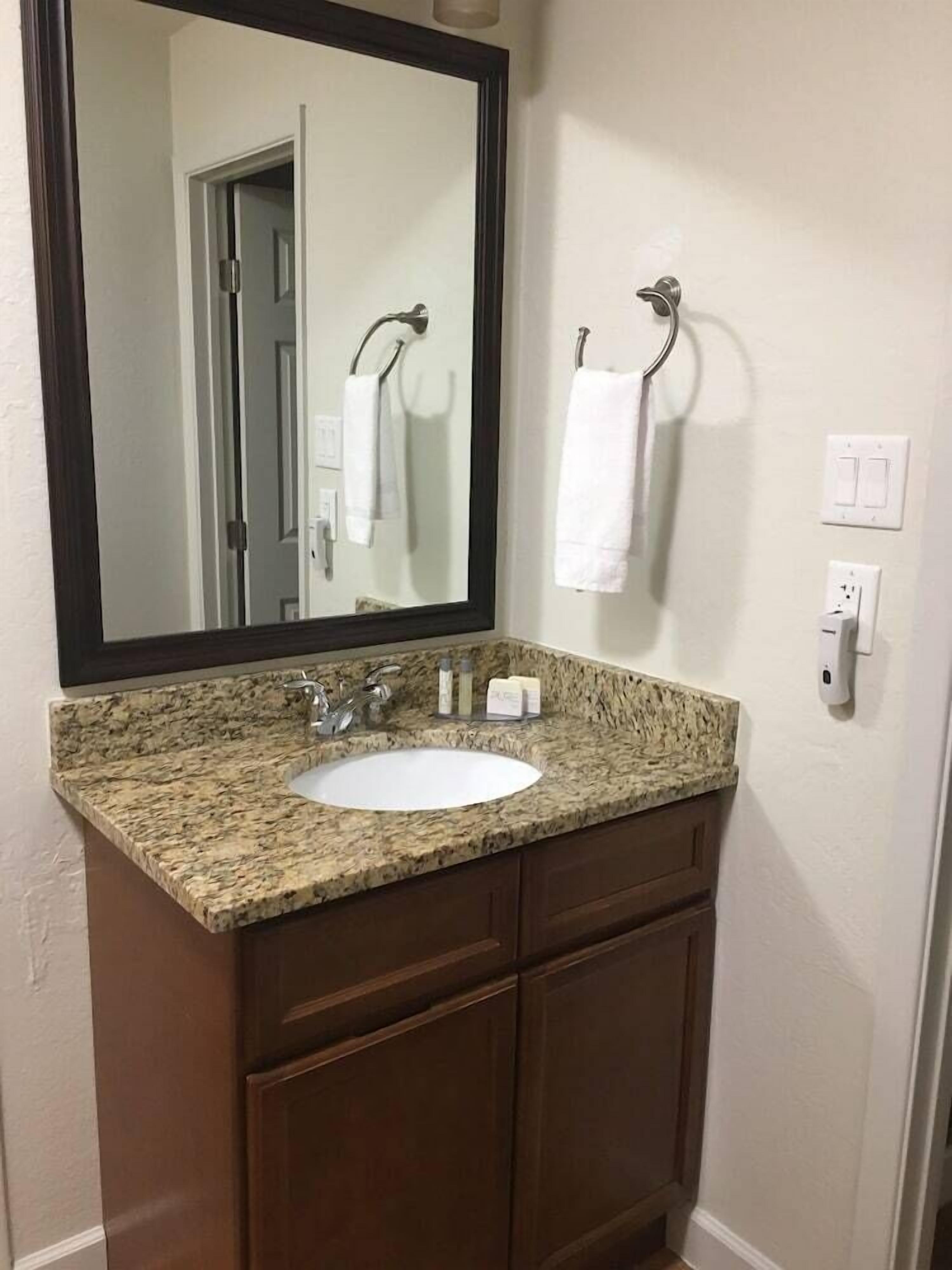 A bathroom with a granite countertop sink, a mirror, and a towel rack.