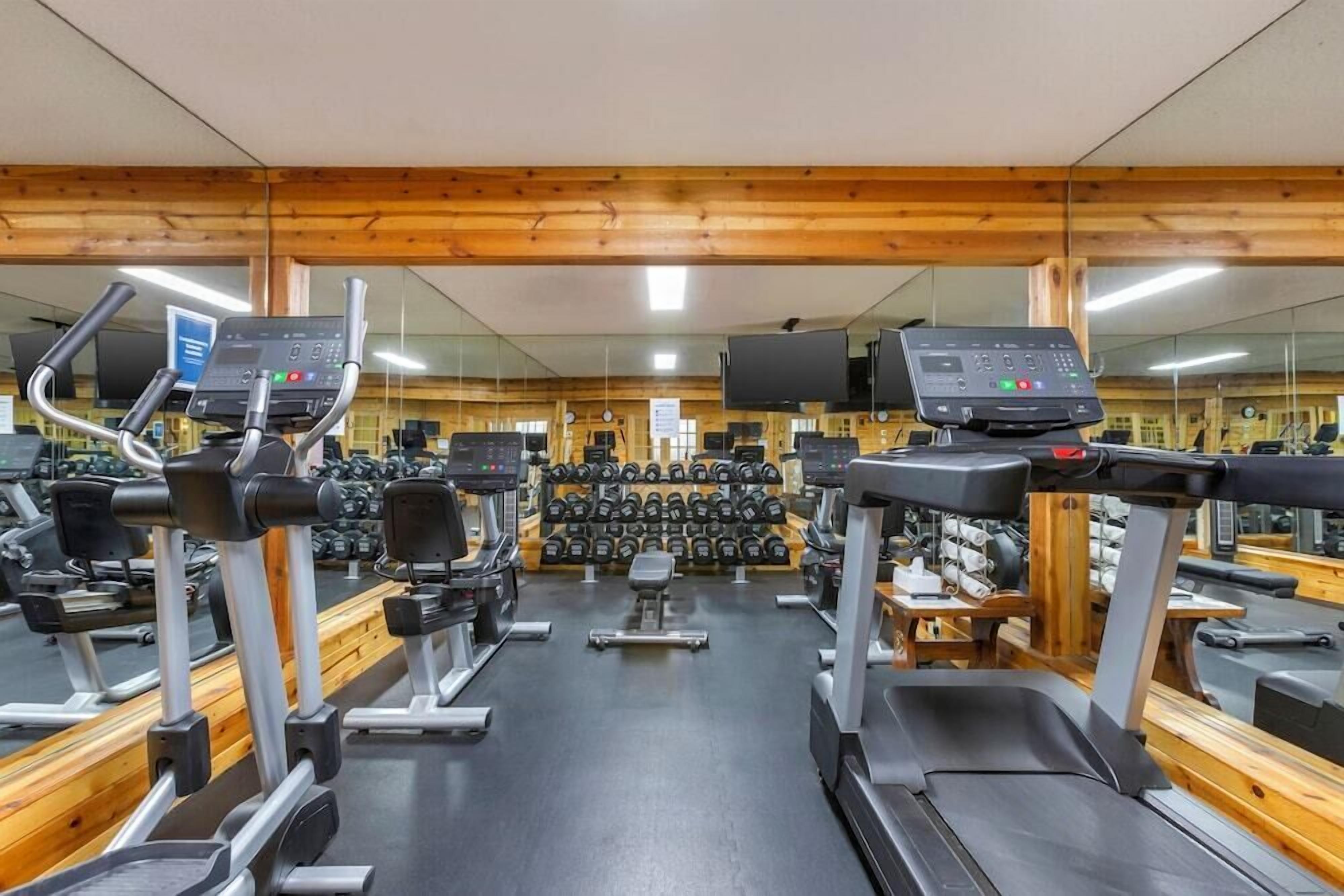 Une salle de sport équipée de tapis de course, de vélos elliptiques et d’une série de haltères.