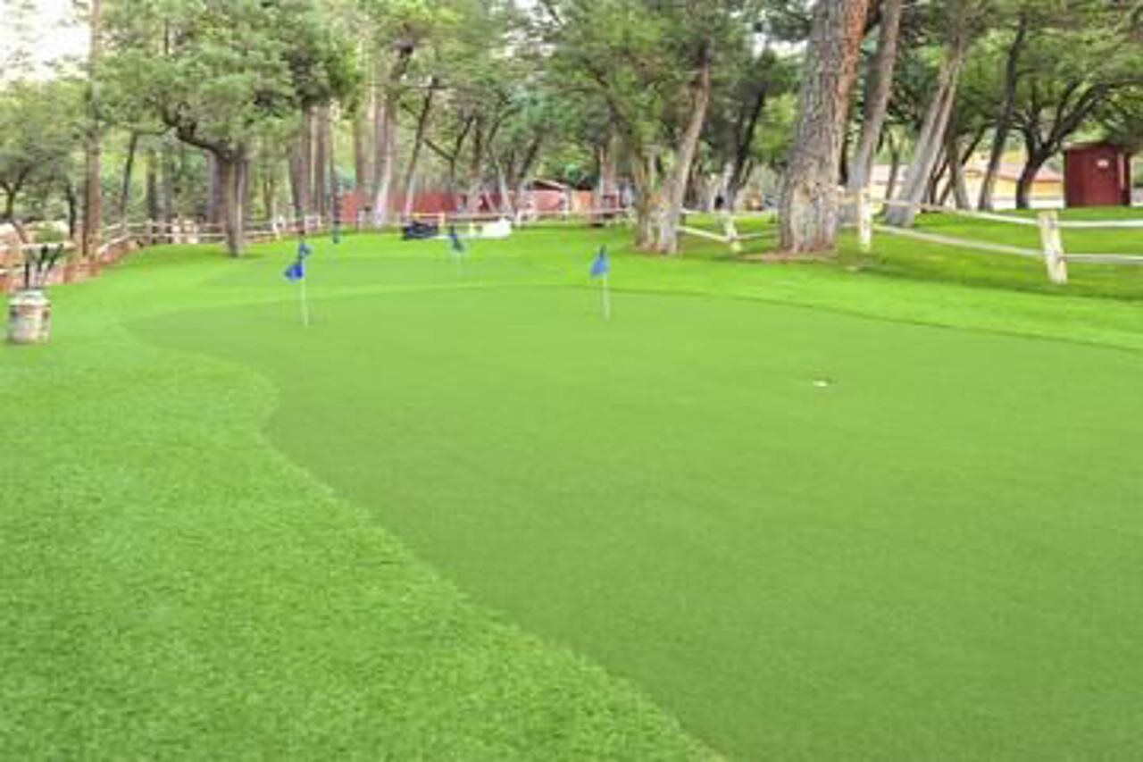 A golf course with a well-maintained green, several flags marking the holes, and a wooden fence surrounding the area.