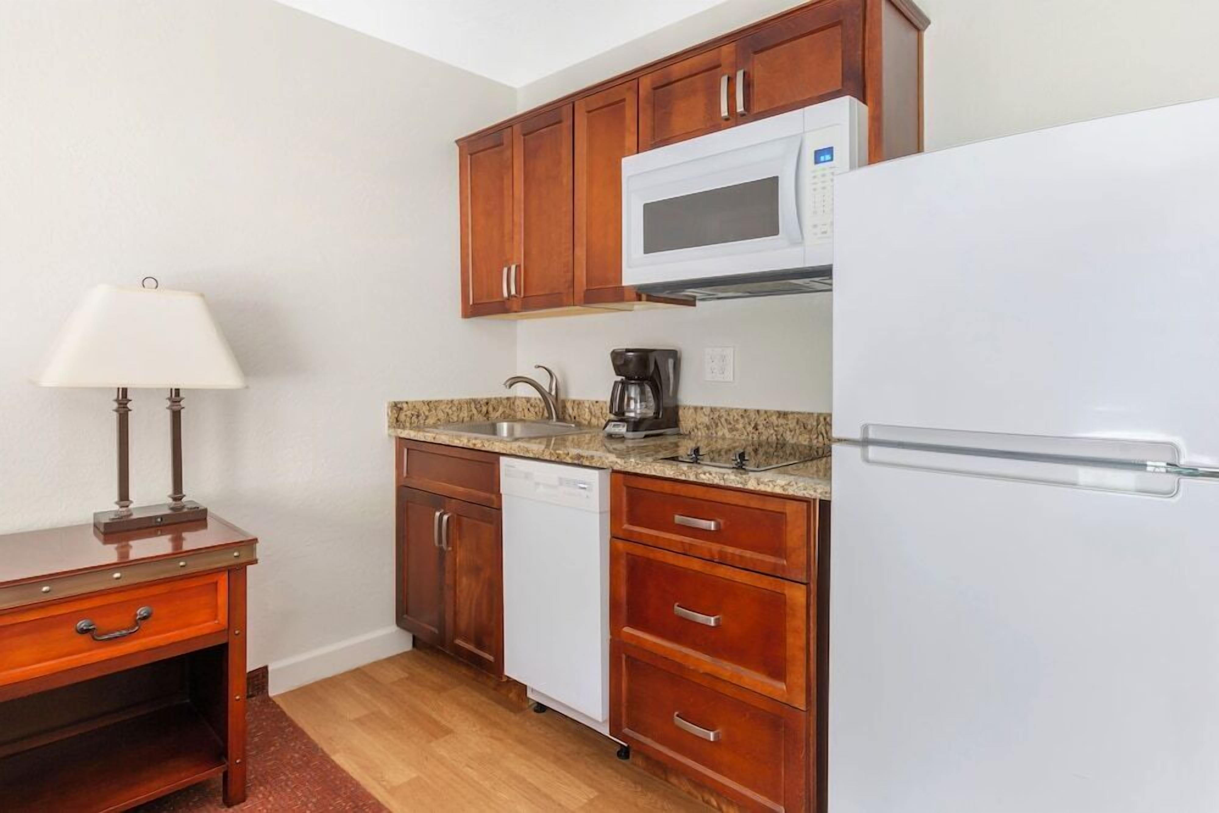 A compact kitchen with wooden cabinets, a white microwave, a coffee maker, and a dishwasher.