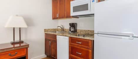 A compact kitchen with wooden cabinets, a white microwave, a coffee maker, and a dishwasher.