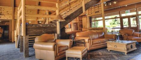 A log cabin interior with leather furniture, a staircase, and large windows.