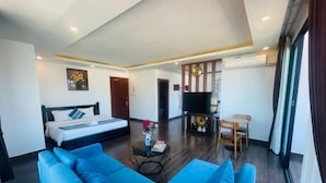A modern hotel room with a large bed, a blue sofa, a small table with a vase, and a TV. - Vang Vieng Topview Hotel (Vang Vieng)