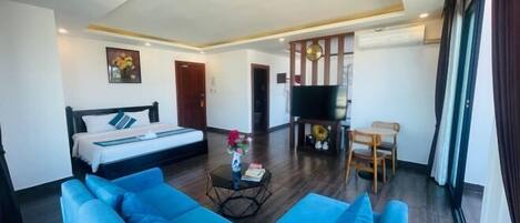 A modern hotel room with a large bed, a blue sofa, a small table with a vase, and a TV.