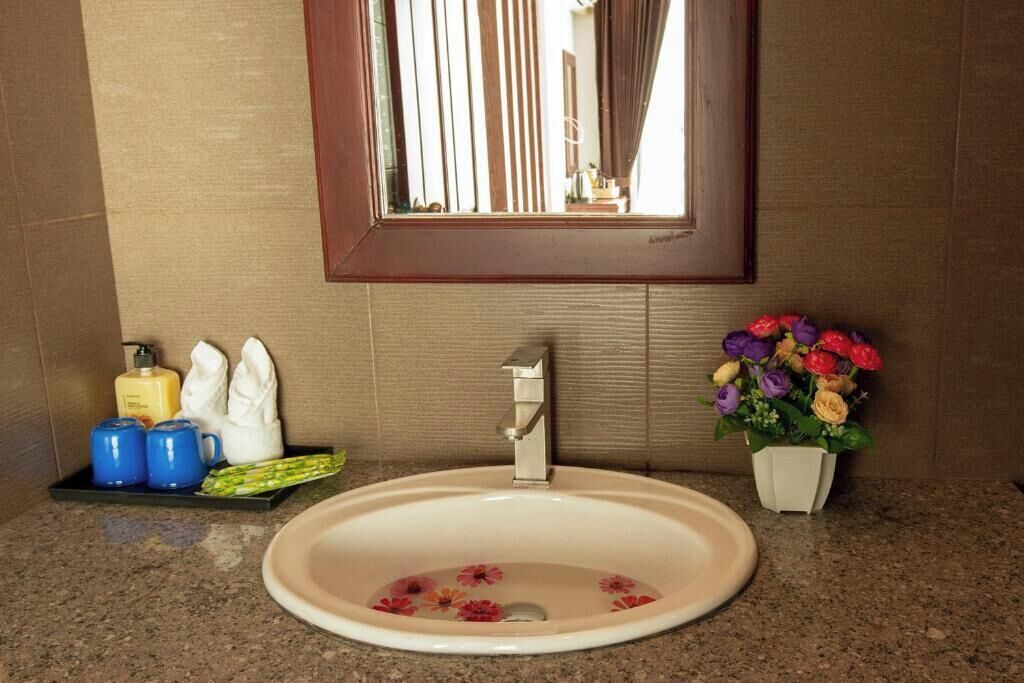 A bathroom with a sink, mirror, toiletries, and a flower arrangement.