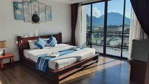 A hotel room with a large bed, a nightstand, a lamp, and a view of mountains through the window. - Vang Vieng Topview Hotel (Vang Vieng)