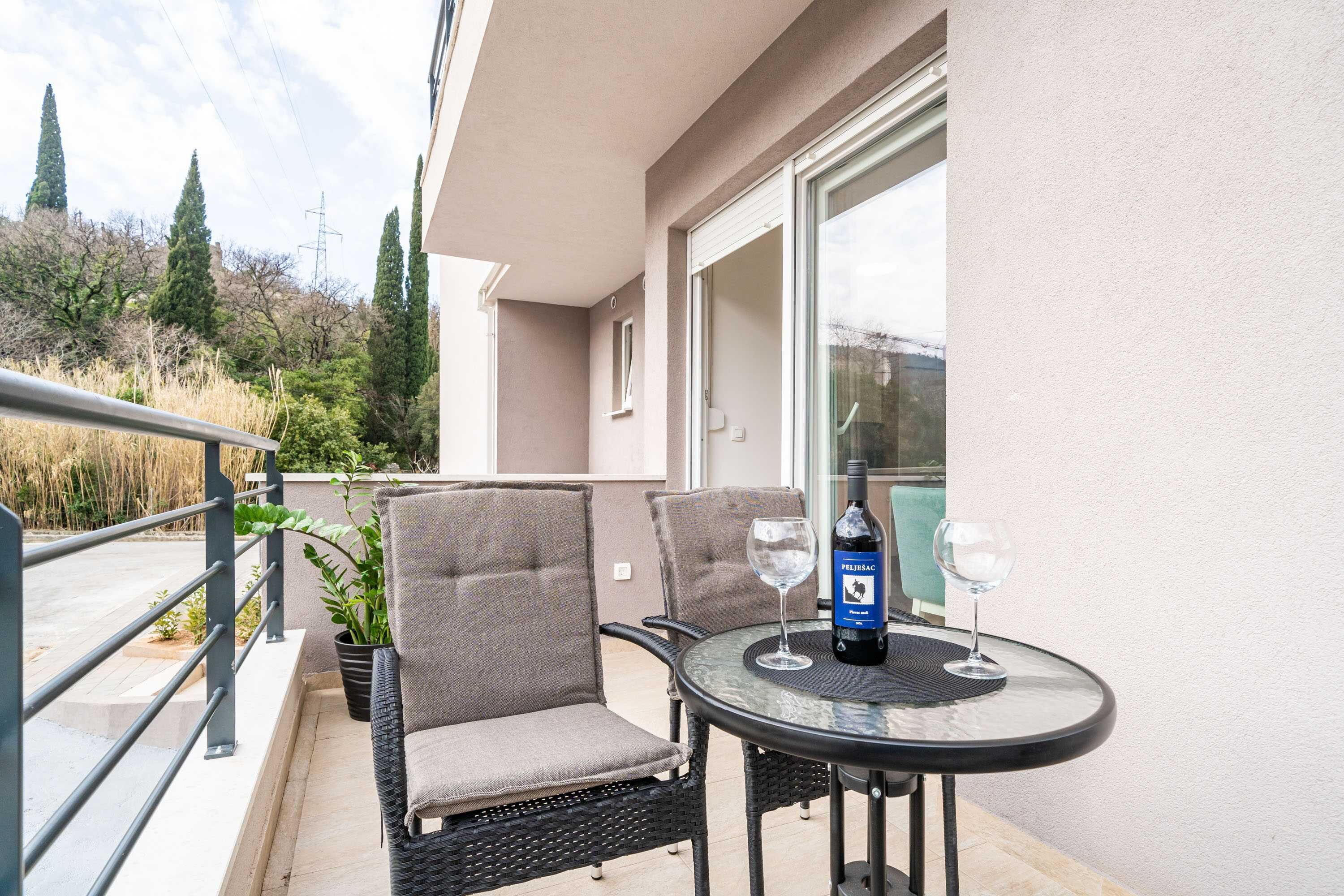 Un balcón con sillones de mimbre, una mesa de vidrio y una botella de vino.