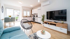 Una sala moderna con un sofá, una zona de comedor con sillas, una cocina con armarios y un televisor en la pared.