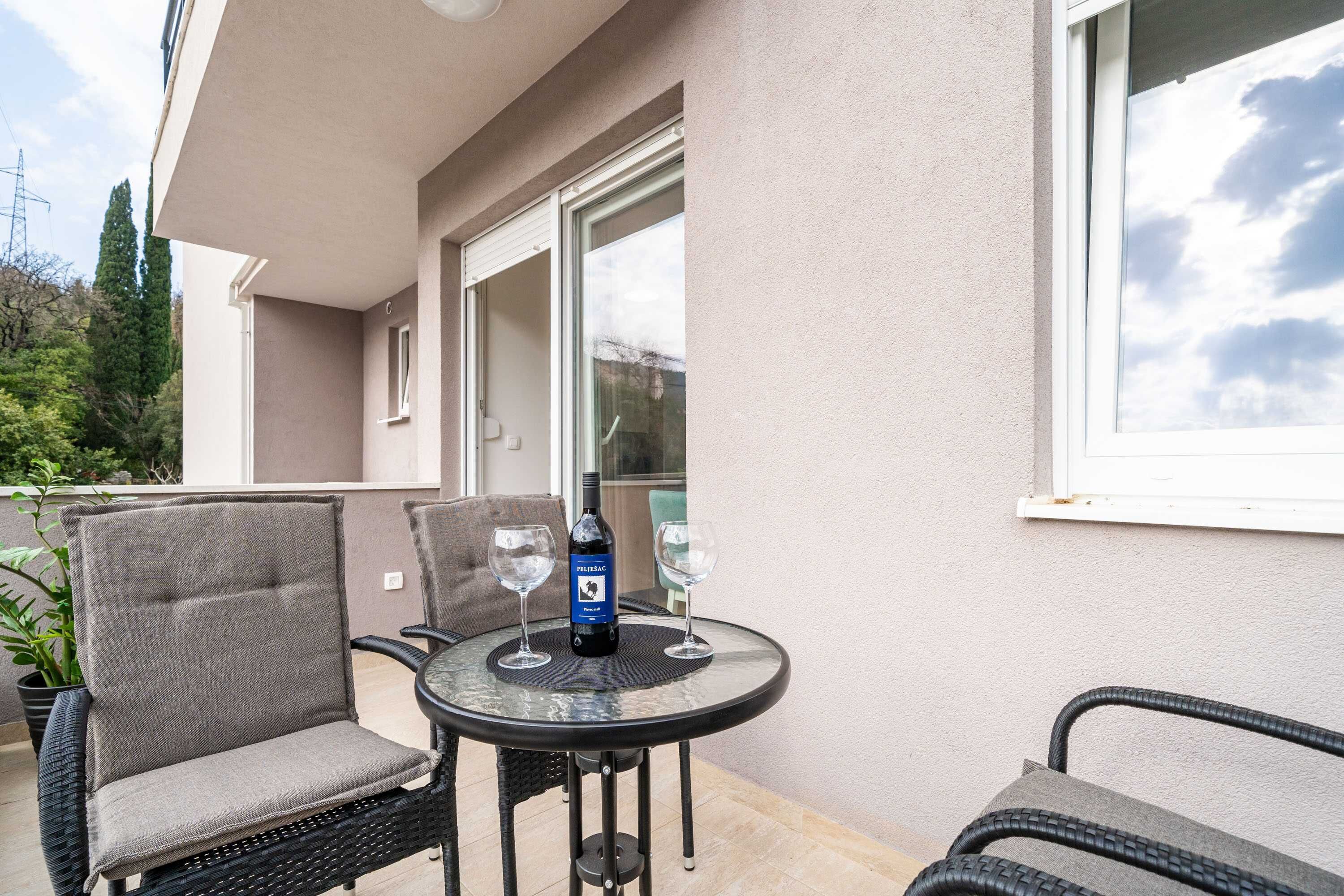 An outdoor patio with a round table, two chairs, a bottle of wine, and two wine glasses.