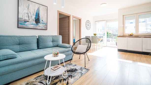 Una sala de estar moderna con un sofá azul, una mesa de centro redonda y un cuadro de barcos de vela.