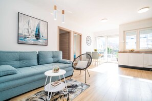 Un salon moderne avec un canapé bleu, une table basse ronde et un tableau représentant des voiliers.