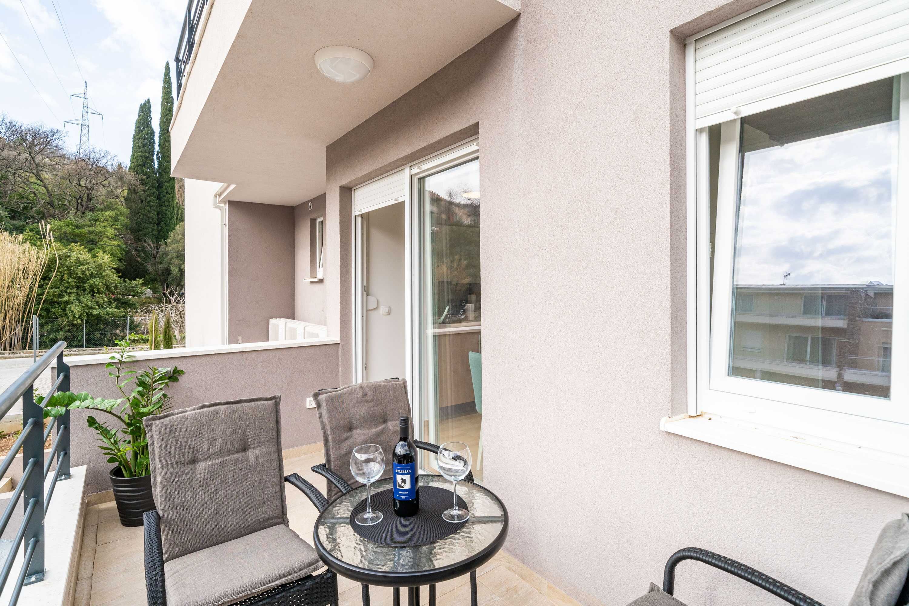 A balcony with a table, two chairs, a bottle of wine, and a potted plant.