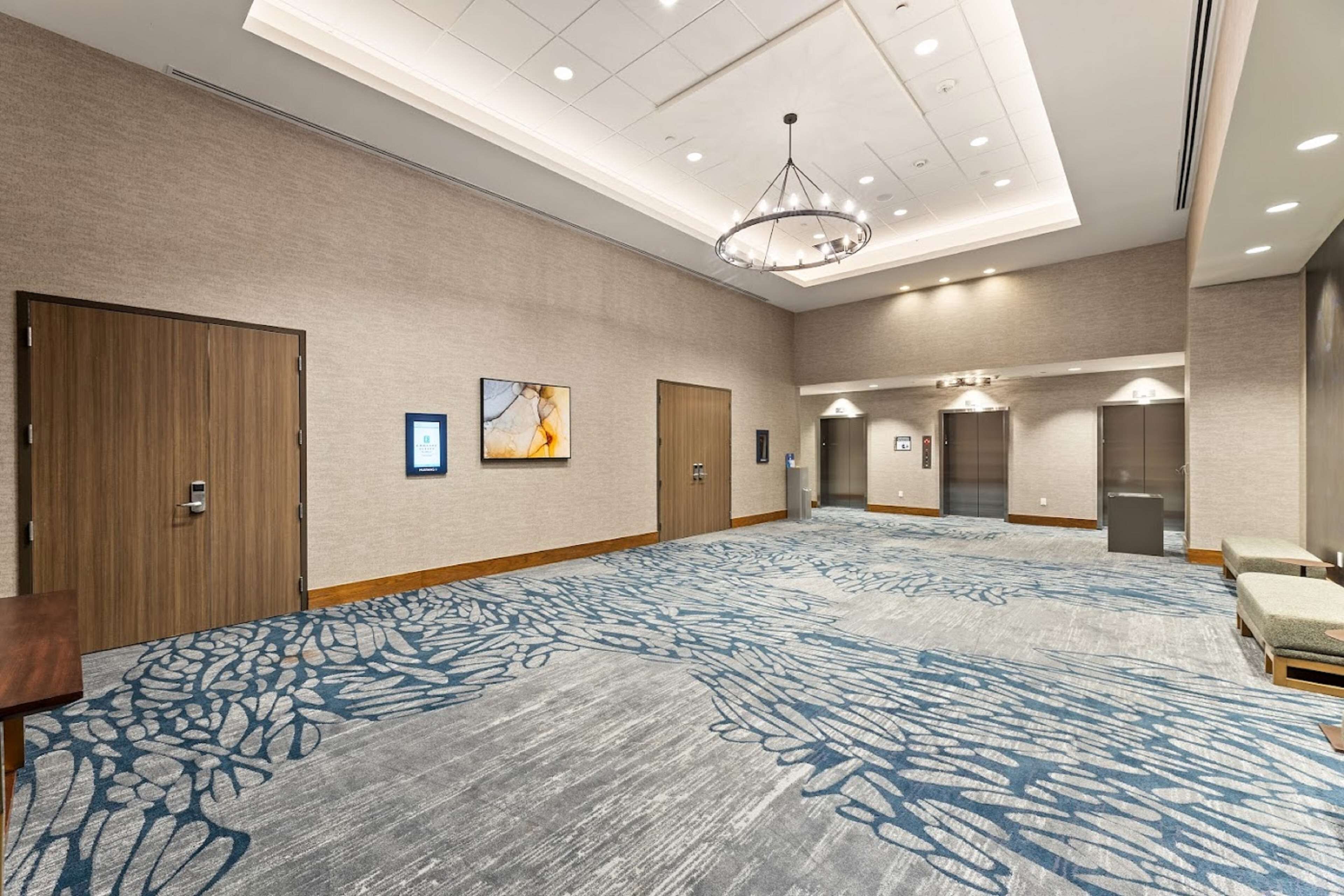 Eine großzügige Hotelhalle mit großem Teppichboden, Holztüren und einem Kronleuchter.