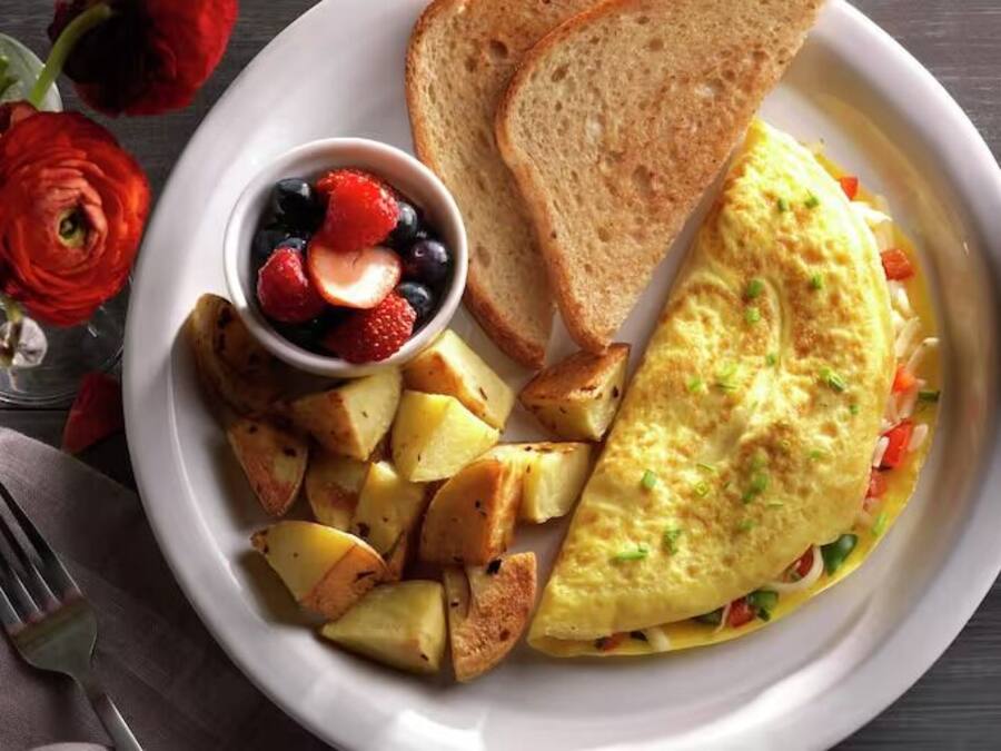 Ein Frühstücksteller mit Toast, Rührei, Kartoffeln und einer kleinen Schüssel Obst.