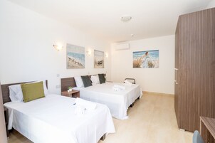 A hotel room with two beds, a wooden wardrobe, and artwork on the walls.