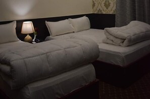 Ein Doppelbett mit weißer Decke und Kissen, ein Nachttisch mit Lampe und wandteppichartige Wandgestaltung.