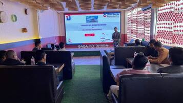 Un salón de conferencias con una pantalla de presentación, asistentes sentados en mesas y un techo decorativo.